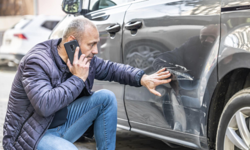 Unfallgeschädigter betrachtet Schden an seinem Auto, nachdem der Verursacher Fahrerflucht begangen hat